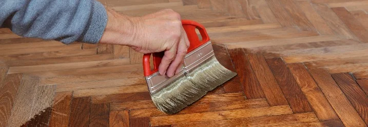 Person trägt Lack auf Parkett auf